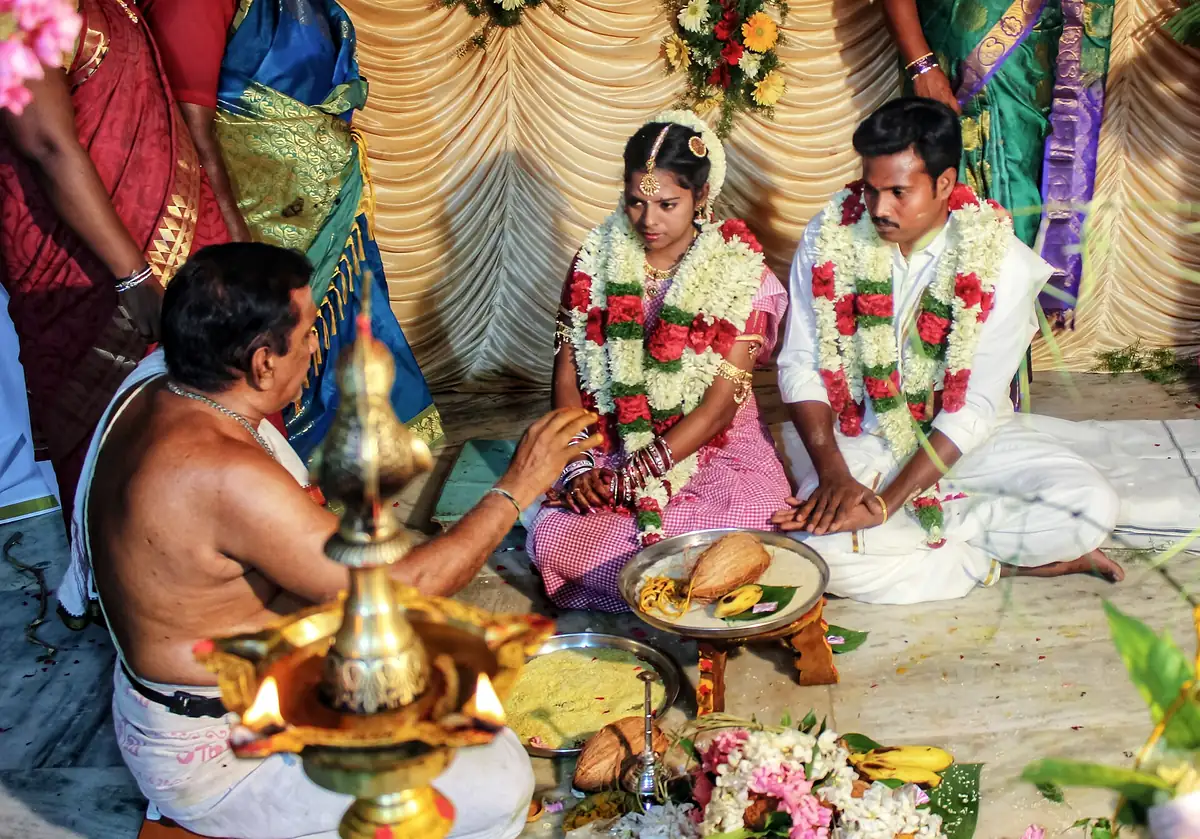 A couple seated at the homam with the priest and a brass lamp in the foreground